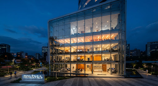 Fachada comercial con muros cortina de vidrio y anclajes de acero inoxidable. Arquitectura moderna al atardecer.